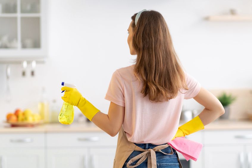 Back view of young lady with cleaning spray ready to tidy her house before guests arrive